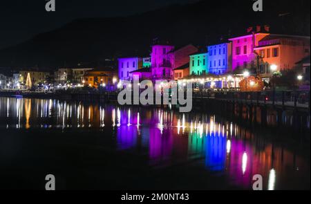 Porto Ceresio, Italie: 12-25-2021: Maisons illuminées par des projecteurs le soir de Noël, par des lumières colorées se reflétant sur l'eau du lac de Luga Banque D'Images