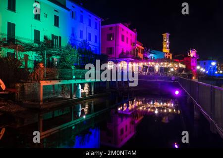 Porto Ceresio, Italie: 12-25-2021: Maisons illuminées par des projecteurs le soir de Noël, par des lumières colorées se reflétant sur l'eau du lac de Luga Banque D'Images