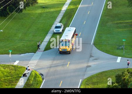 Vue de dessus de l'école de bus jaune américain standard qui prend les enfants à l'arrêt de rue de ville rurale pour leurs propres cours en début de matinée. Les transports publics dans le Banque D'Images