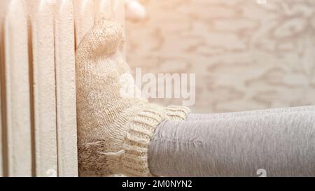 Femme en chaussettes tricotées chaudes chauffe ses jambes sur le radiateur. Banque D'Images
