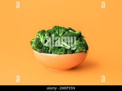 Bol avec brocoli bouilli minimaliste sur une table orange. Gros plan avec du brocoli vert cuit dans un bol d'orange. Plat végétalien sain. Banque D'Images