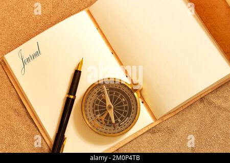 Journal en cuir, avec le mot journal sur une page, avec un stylo plume et une boussole antique dans le sable. Concept de journal de voyage Banque D'Images