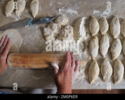 vue de dessus de la table de cuisine maison et les mains de femmes roulant de pâte avec broche en bois dans le processus de fabrication de tartes de viande maison Banque D'Images