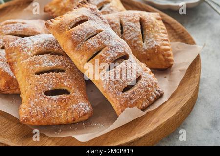 Tourtes à main. Mini-pâte feuilletée ou tartes farcies aux pommes et saupoudrées de sucre en poudre dans une assiette de bois. En-cas à tarte maison avec croûte pour le petit déjeuner rus Banque D'Images