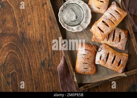 Tourtes à main. Mini-pâte feuilletée ou tartes farcies aux pommes et saupoudrées de sucre en poudre dans une assiette de bois. En-cas à tarte maison avec croûte pour le petit déjeuner rus Banque D'Images