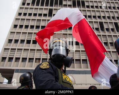 Pérou, 07/12/2022, la police de Riot avec masque à gaz sous un drapeau péruvien quand des centaines de citoyens, certains enveloppés dans le drapeau péruvien, prennent dans les rues pour célébrer le retrait du Président Pedro Castillo. Castillo a été destitué par le Congrès pour "l'incapacité orale" après avoir tenté un coup d'Etat manqué qui a cherché à fermer le Congrès et le pouvoir judiciaire. Banque D'Images