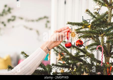 Femme main avec tatouage sur elle, décorant l'arbre de Noël avec des ornements rouges Banque D'Images