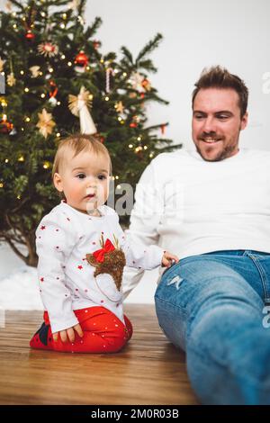 Bébé fille et son père en tenue de Noël festive assis près de l'arbre de Noël Banque D'Images