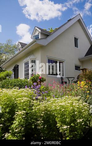 Maison de style Canadiana de style manoir français à deux étages des années 1950 avec bordure noire et jardin paysager en été. Banque D'Images