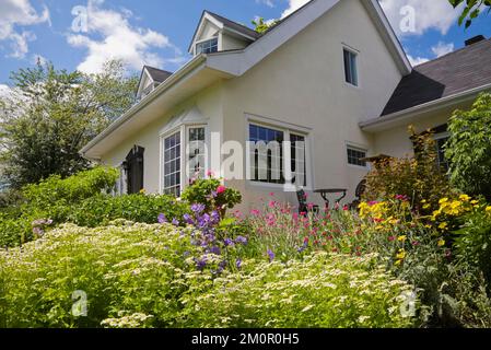 Maison de style Canadiana de style manoir français à deux étages des années 1950 avec bordure noire et jardin paysager en été. Banque D'Images