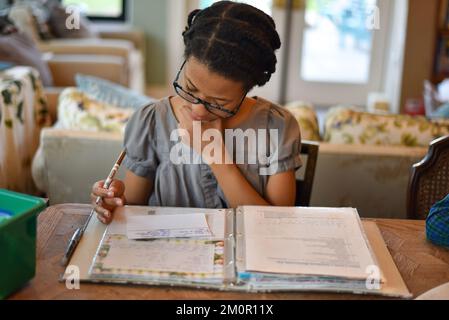 Jeune fille faisant des devoirs à la maison tout en étant assis à la table de cuisine écrivant sur un cahier d'exercices Banque D'Images
