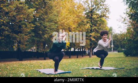 La jeune fille mince élève de yoga apprend Eagle pose sous la direction d'un enseignant expérimenté pendant la pratique individuelle avec un instructeur dans le parc. Belle nature d'automne est en arrière-plan. Banque D'Images