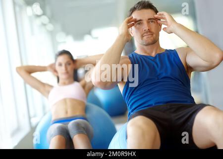 Se sentir sous tension. Deux personnes faisant des exercices sur des balles suisses à la salle de gym. Banque D'Images