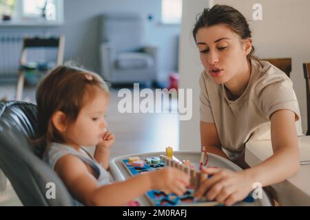 Bonne petite fille de bébé jouant avec le jouet en bois coloré apprendre à compter en jouant avec sa mère à la maison. Enseignement des numéros à la maison. Enfance Banque D'Images