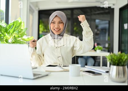 Une jeune femme de bureau musulmane asiatique heureuse et joyeuse se fait la main, célébrant son succès, recevant de bonnes nouvelles, obtenant une promotion d'emploi. Banque D'Images