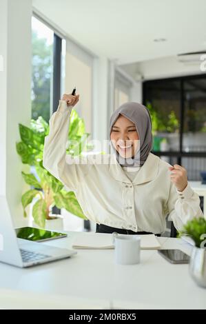 Portrait, une jeune femme musulmane asiatique heureuse et gaie fait la main, célébrant son succès et recevant de bonnes nouvelles. Banque D'Images