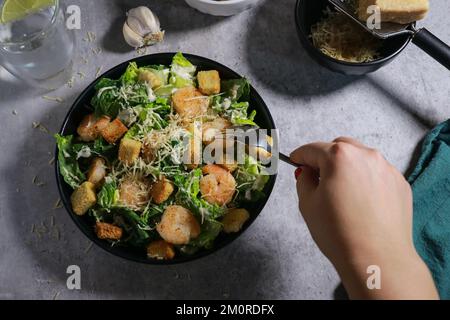 Gros plan de la femme mangeant de la salade César à la fourchette sur une table en marbre gris Banque D'Images