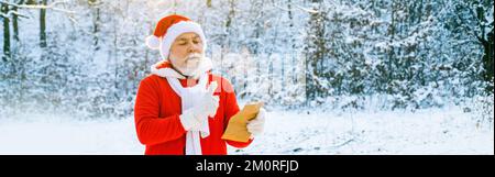 Le Père Noël lisant la lettre de noël au père noël. Lettre de lecture du Père Noël au Père Noël sur forêt naturelle de neige, bannière. Banque D'Images