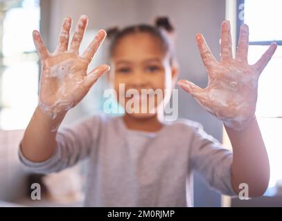 Une petite fille se lavant les mains avec de l'eau et du savon dans une salle de bains. Joyeux enfant montrant des palmiers savonneux. Hygiène des mains et protection contre les virus. Fille afro-américaine Banque D'Images