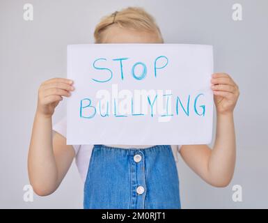 Une petite fille triste et malheureuse tenant un panneau d'arrêt d'intimidation. Adorable petite fille d'âge élémentaire qui a peur tout en cachant son visage et en protestant Banque D'Images