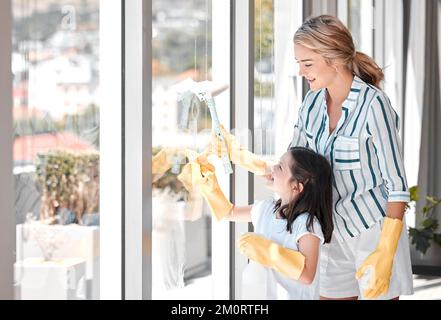 Bonne jeune mère nettoyait les fenêtres avec sa fille à l'aide d'une raclette. Nettoyage de parents souriants, travaux ménagers corvées avec son enfant pendant Banque D'Images