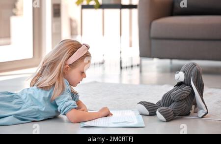 Petite fille lisant un livre d'histoire à la maison avec teddybear. Adorable fille caucasienne couchée sur le sol et lisant une histoire à son animal en peluche Banque D'Images