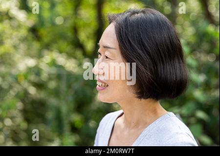 Vue de côté d'une femme asiatique-américaine senior debout à l'extérieur Banque D'Images