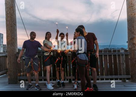 Jeune groupe de grimpeurs de rock qualifiés ayant du plaisir et jouant avec des sparkles avec le coucher du soleil en arrière-plan Banque D'Images