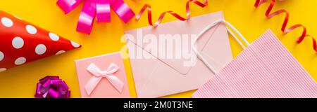 Vue de dessus de la casquette de fête près du cadeau et de l'enveloppe sur fond jaune, bannière, image de stock Banque D'Images