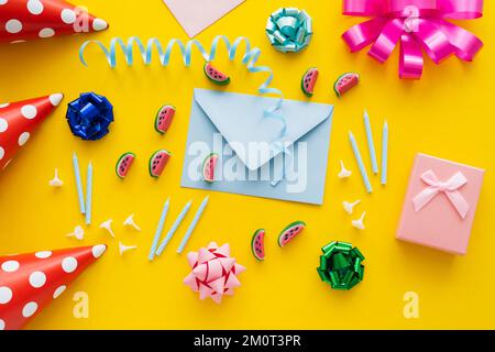 Vue de dessus du présent près de l'enveloppe et des capuchons de fête sur fond jaune, image de stock Banque D'Images