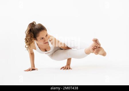 Une jeune femme menant un mode de vie sain et pratiquant le yoga, exécute l'exercice Ashtavakrasana, balance asana, stand, s'entraîne en sport blanc Banque D'Images