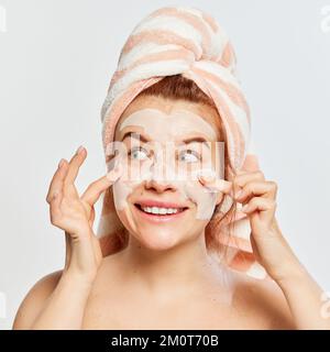 Portrait de jeune, belle, rouge-cheveux femme appliquant le masque d'argile du visage après la douche isolé sur fond blanc Banque D'Images