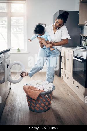 Le linge de bébé ne peut pas attendre. une jeune mère utilisant un téléphone portable tout en effectuant des travaux ménagers et en tenant son bébé à la maison. Banque D'Images