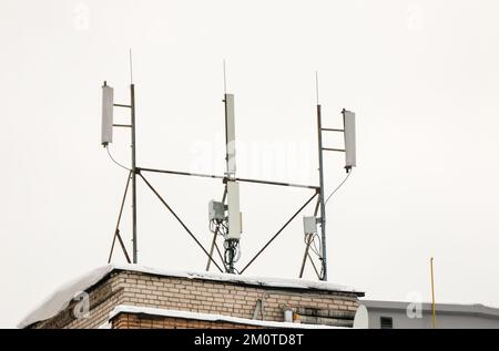 Plusieurs antennes cellulaires sur le toit de la maison fournissent la communication. La neige se trouve sur le jalon, sur fond de ciel gris. Nuageux, froid jour d'hiver, lumière douce. Banque D'Images