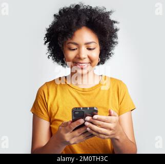 Mi accroché à cette application cool. une femme utilisant son téléphone portable tout en posant sur un fond gris. Banque D'Images