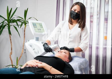 Kiev, Ukraine - 26 décembre 2020: Jeune esthéticienne faisant le nettoyage du visage pour le patient, en utilisant Ultraformer. Concept de procédure pour améliorer la peau pendant la période de quarantaine. Banque D'Images