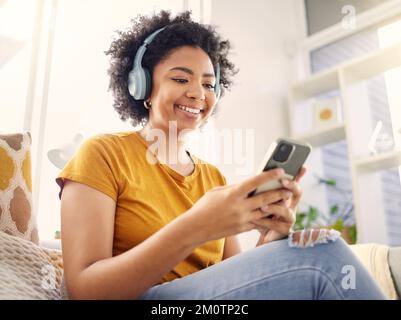 C'est toujours agréable de rattraper son retard. une jeune femme utilisant un téléphone tout en écoutant de la musique à la maison. Banque D'Images