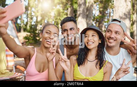 Montrer où nous en sommes sur les réseaux sociaux. un groupe diversifié d'amis se tenant ensemble et prenant des selfies sur un téléphone portable tout en campant dans les bois. Banque D'Images