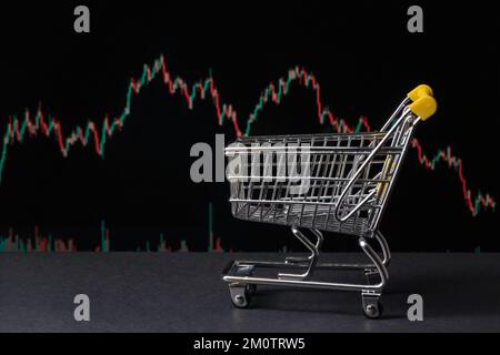 Achat de stocks ou crypto sur un échange. Panier sur fond noir à côté d'un tableau de prix Banque D'Images