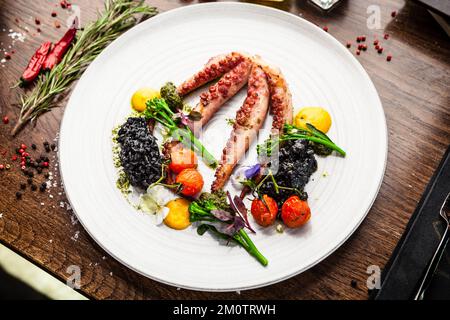 Poulpe avec risotto noir. Crème de carottes, mini-brocoli, pesto de basilic. Une délicieuse cuisine traditionnelle saine est servie pour le déjeuner dans une cuisine gastronomique moderne Banque D'Images