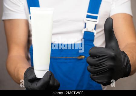 Gros plan l'employé en uniforme bleu et T-shirt blanc tient le tube blanc sur lequel vous pouvez placer le logo ou le texte. Espace pour la copie. Banque D'Images