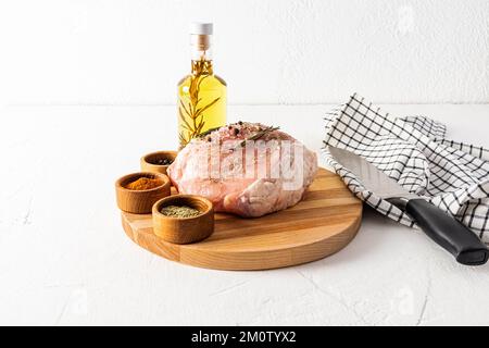 viande de porc crue sur une planche à découper ronde avec des bols de différentes épices et de l'huile de romarin pour la cuisson. le concept de la cuisson de la viande Banque D'Images