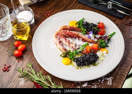 Poulpe avec risotto noir. Crème de carottes, mini-brocoli, pesto de basilic. Une délicieuse cuisine traditionnelle saine est servie pour le déjeuner dans une cuisine gastronomique moderne Banque D'Images