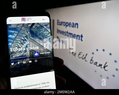 Personne tenant un téléphone portable avec page web de l'institution de l'UE Banque européenne d'investissement (BEI) à l'écran avec logo. Concentrez-vous sur le centre de l'écran du téléphone. Banque D'Images