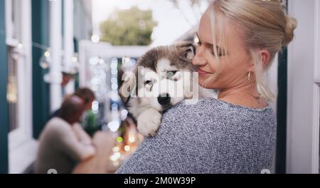 Femme tenant son chien avec amour, soin et bonheur lors d'un dîner, d'une fête ou d'une célébration dans une maison. Bonne, souriante et femme qui embrasse son animal husky à un Banque D'Images