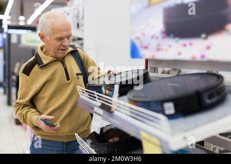 homme âgé qui choisit un robot-aspirateur dans la salle d'exposition du magasin d'appareils électriques Banque D'Images