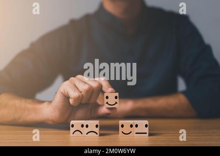 meilleur excellent service d'affaires pour évaluer l'expérience client. Concept d'enquête de satisfaction. Main d'un homme d'affaires choisit une smiley visage sur le bloc de bois cu Banque D'Images