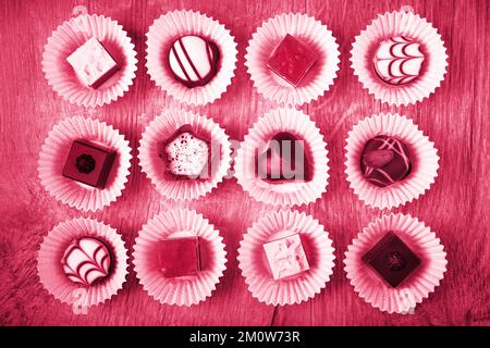 Viva Magenta couleur de l'année 2023. Vue de dessus sur les pralines de chocolat variées sur le bois Banque D'Images