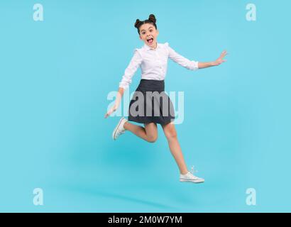 Joyeux drôle de saut adolescent. Bonne écolière, émotions positives et souriantes de la jeune fille. Saut en longueur d'une adolescente sur un studio isolé bleu Banque D'Images