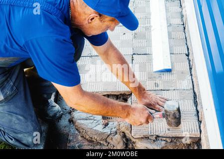 Le calque de briques pose des carreaux. Un constructeur professionnel en combinaison et casquette de baseball au travail. Maçon âgé travaillant à l'extérieur. Gros plan... Banque D'Images